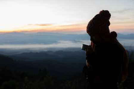 Young woman is enjoying cup of coffee outside with beautiful view of mountainsの写真素材