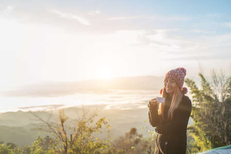 Young woman is enjoying cup of coffee outside with beautiful view of mountainsの写真素材