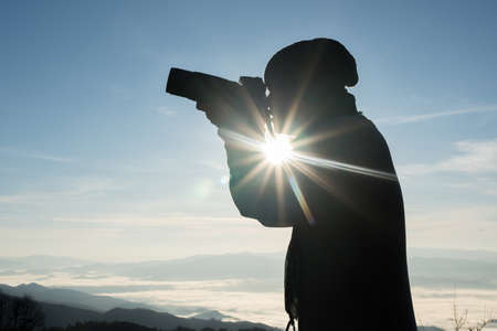 Silhouette  young photographer holding a camera with landscape in the mountain.の写真素材