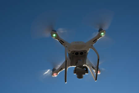 White drone hovering in a bright blue sky