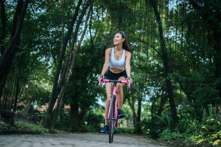 Woman riding a road bike in the park. Portrait of young beautiful woman on pink bike.の写真素材