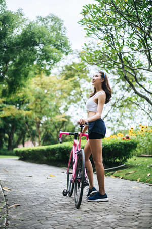 Portrait of young beautiful woman with pink bike in the park. Actractive healthy woman.の写真素材