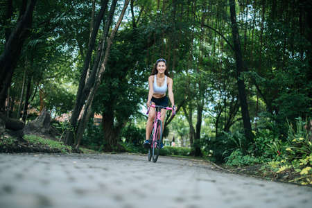 Woman riding a road bike in the park. Portrait of young beautiful woman on pink bike.の写真素材
