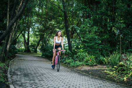 Woman riding a road bike in the park. Portrait of young beautiful woman on pink bike.の写真素材
