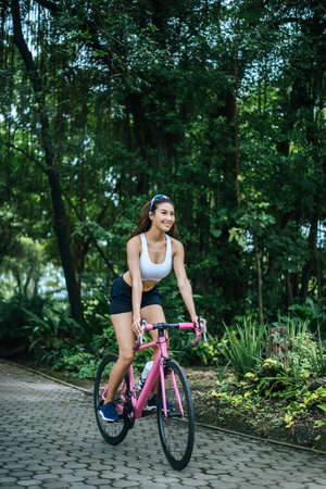 Woman riding a road bike in the park. Portrait of young beautiful woman on pink bike.の写真素材