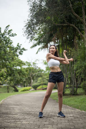 Young sport woman runner stretching body before run on track in the park.の写真素材