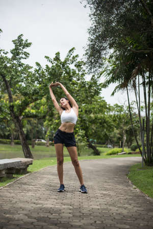 Young sport woman runner stretching body before run on track in the park.の写真素材