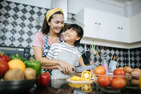 Happy mom teaching her daughter preparing and chopping vegetable  for cooking.の写真素材