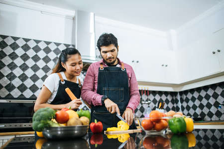 Happy young couple help each other chopping vegetable preparing for cooking in kitchen at home.の写真素材