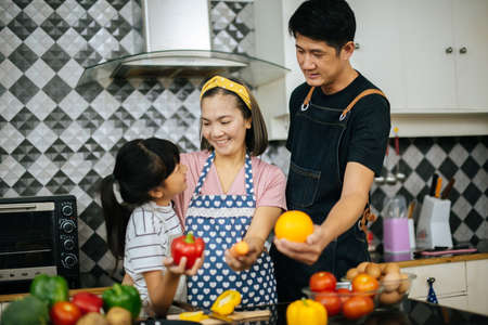Cute girl help her parents are cutting vegetables and smiling while cooking together in kitchen at home.の写真素材