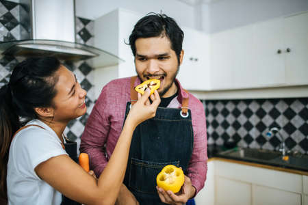Happy young couple help each other chopping vegetable preparing for cooking in kitchen at home.の写真素材