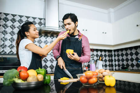 Happy young couple help each other chopping vegetable preparing for cooking in kitchen at home.の写真素材