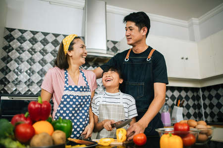 Cute girl help her parents are cutting vegetables and smiling while cooking together in kitchen at home.の写真素材