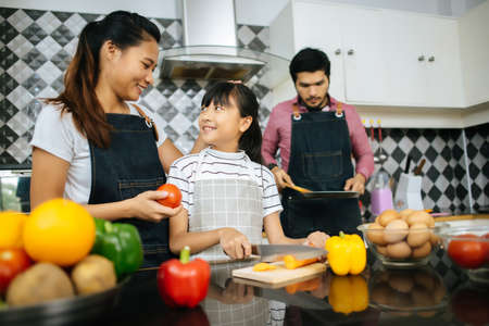 Family cooking time : Happy mum teach her daughter chopping vegetable preparing ingredients for cooking meal in kitchen at home.の写真素材