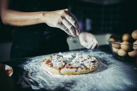 Chef hands pouring flour powder on raw dough. Cooking concept.の写真素材