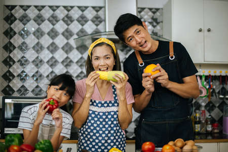 Cute girl help her parents are cutting vegetables and smiling while cooking together in kitchen at home.の写真素材