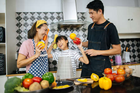 Cute girl help her parents are cutting vegetables and smiling while cooking together in kitchen at home.の写真素材