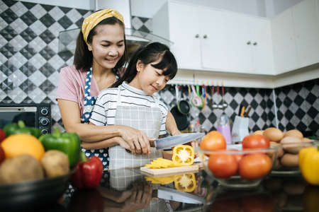 Happy mom teaching her daughter preparing and chopping vegetable  for cooking.の写真素材