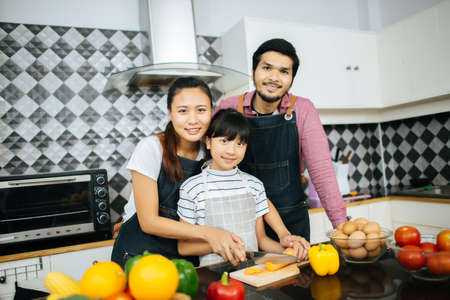 Family cooking time : Happy mum teach her daughter chopping vegetable preparing ingredients for cooking meal in kitchen at home.の写真素材