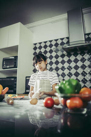 Cute little girl kneads flour dough preparing for make pizza. Cooking concept.の写真素材