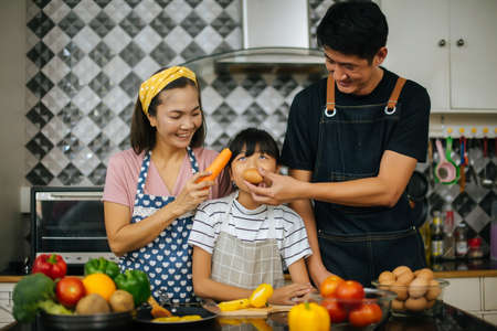 Cute girl help her parents are cutting vegetables and smiling while cooking together in kitchen at home.の写真素材