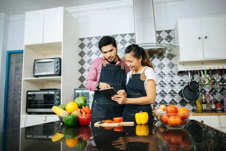 Happy young couple is using digital tablet to looking method to cooking while cooking in kitchen at home.の写真素材