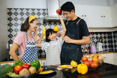 Cute girl help her parents are cutting vegetables and smiling while cooking together in kitchen at home.の写真素材