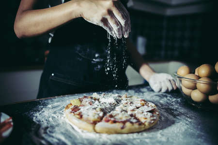 Chef hands pouring flour powder on raw dough. Cooking concept.の写真素材