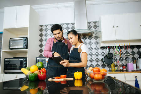 Happy young couple is using digital tablet to looking method to cooking while cooking in kitchen at home.の写真素材