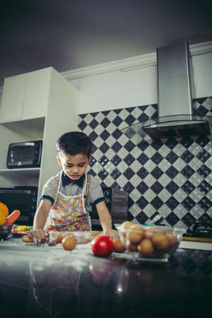 Cute Little boy learn how to cook standing in the kitchen at home.の写真素材