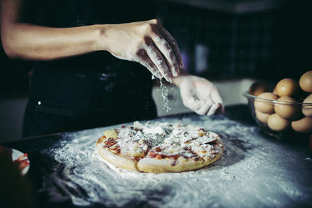 Chef hands pouring flour powder on raw dough. Cooking concept.の写真素材
