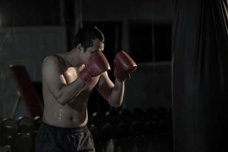 Portrait of a young asian man practicing boxing on a punching bag at gym.の写真素材