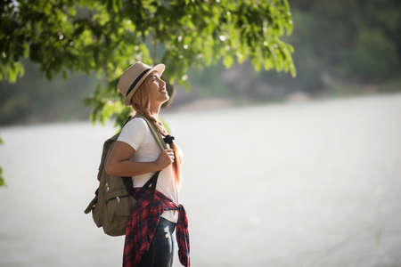 Young happy woman with backpack standing looking to the river. Woman traveling concept.の写真素材