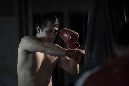 Portrait of a young asian man practicing boxing on a punching bag at gym.の写真素材