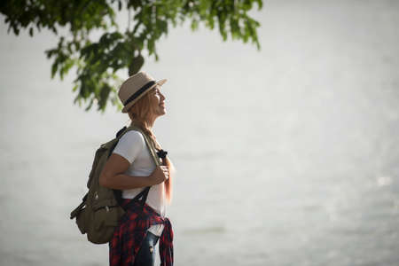 Young happy woman with backpack standing looking to the river. Woman traveling concept.の写真素材