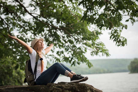 Young happy woman sitting with backpack enjoy the nature after hike. Woman travel concept.の写真素材