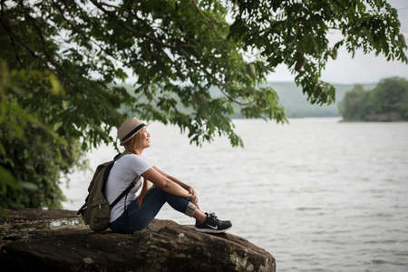 Young happy woman sitting with backpack enjoy the nature after hike. Woman travel concept.の写真素材