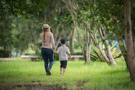 Rear view of mother and son walking together in home garden holding hand. Family concept.の写真素材