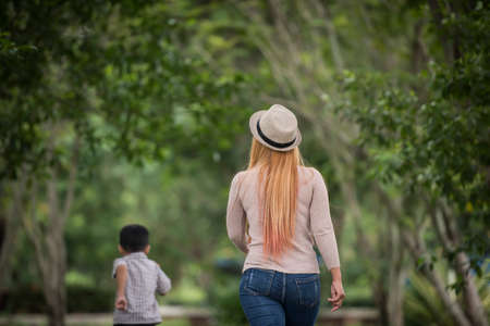 Rear view of mother and son walking together in home garden holding hand. Family concept.の写真素材
