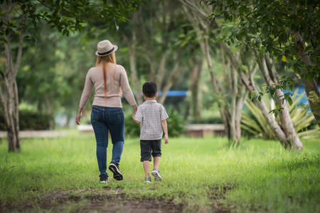 Rear view of mother and son walking together in home garden holding hand. Family concept.の写真素材
