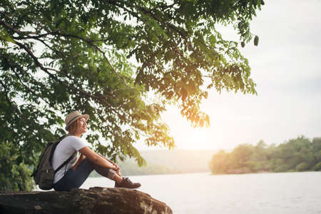 Young happy woman sitting with backpack enjoy the nature after hike. Woman travel concept.の写真素材