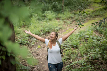 Young woman with backpack and raised up arms while walking through the forest.の写真素材