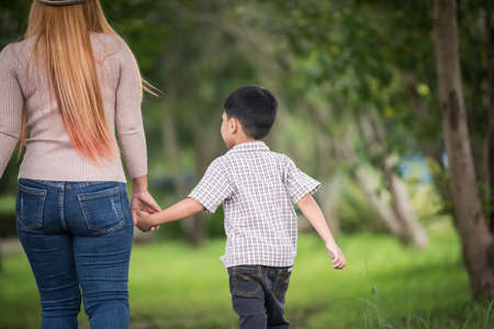 Rear view of mother and son walking together in home garden holding hand. Family concept.の写真素材