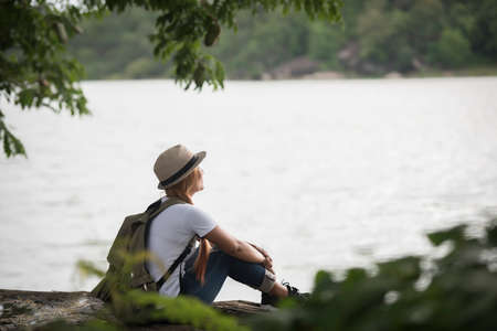 Young happy woman sitting with backpack enjoy the nature after hike. Woman travel concept.の写真素材
