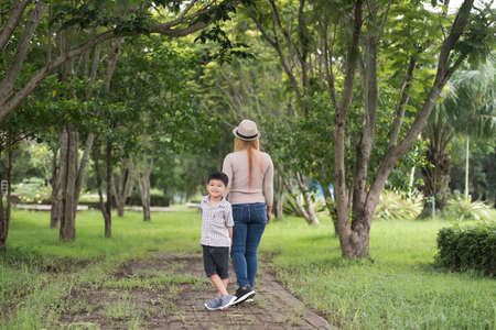 Rear view of mother and son walking together in home garden holding hand. Family concept.の写真素材