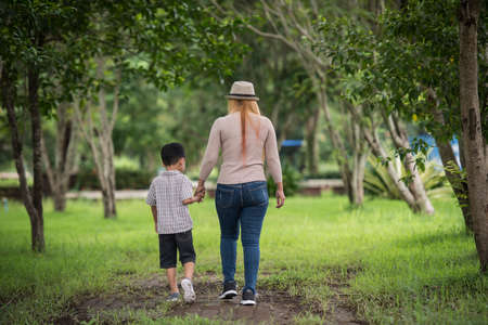 Rear view of mother and son walking together in home garden holding hand. Family concept.の写真素材