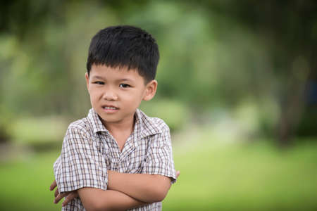 Portrait of cute little curious boy standing with arms folded and looking at camera with blurred nature background.の写真素材