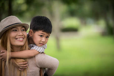 Happy young mother and son laughing little boy getting a piggyback ride on her back. Family concept.の写真素材