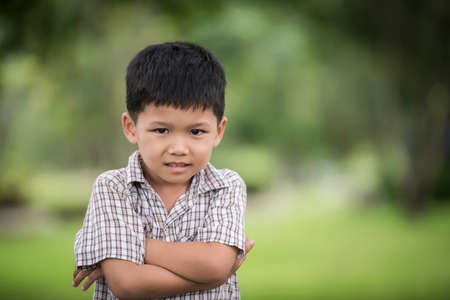Portrait of cute little curious boy standing with arms folded and looking at camera with blurred nature background.の写真素材