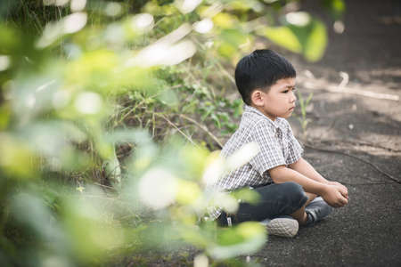 Cute little boy sitting on the ground in the summer park.の写真素材